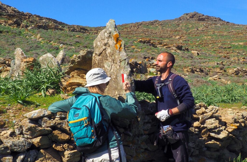Paths of Greece Waymarking in Tinos Field team member from Paths of Greece painting a trail waymarker on a stone wall in Tinos - Hike Greece